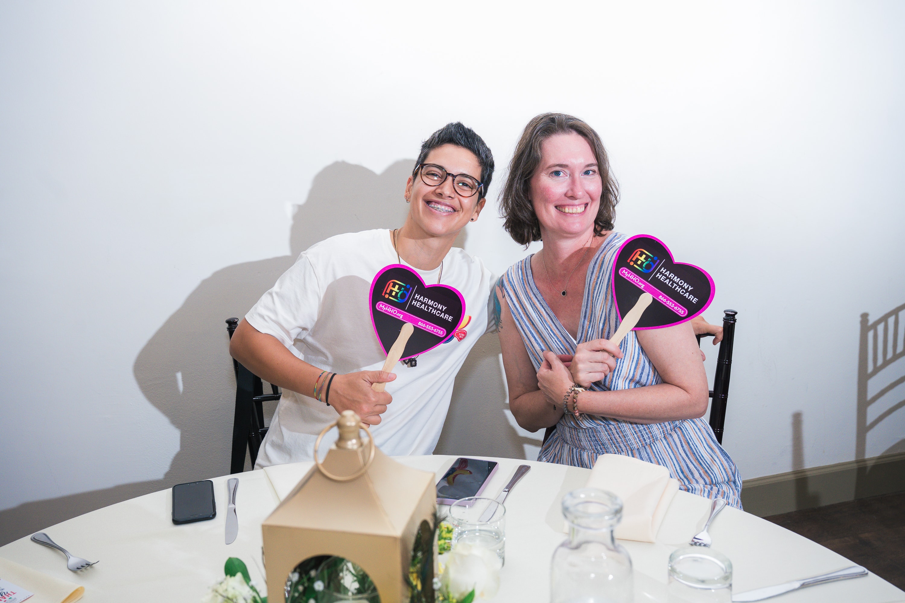Two guests holding Harmony Healthcare fans at Peacocks & Divas 2025