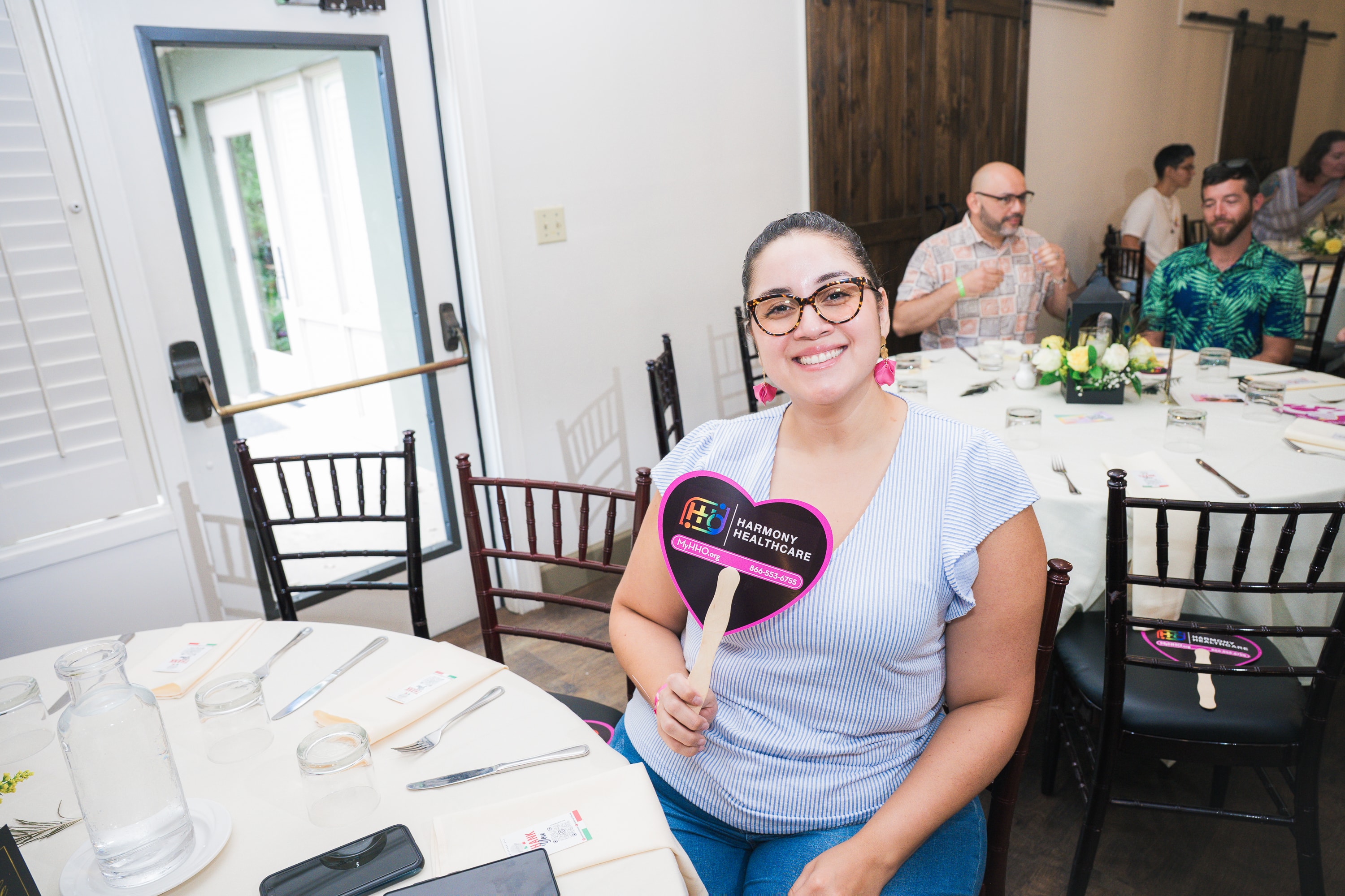 Guest holding a Harmony Healthcare fan at Peacocks & Divas 2025